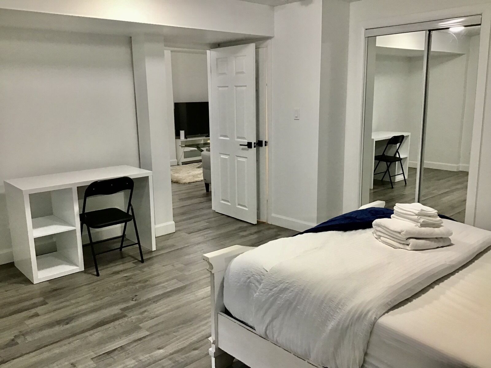 Un dormitorio con cama, escritorio, silla, armario y televisor al fondo.