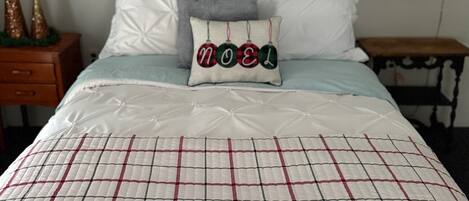 A bedroom with a bed, pillows, a quilt, a wall art piece, and a small table with a lamp.
