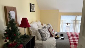 Une chambre à coucher avec un lit, une table de chevet, un sapin de Noël et une fenêtre avec des rideaux.