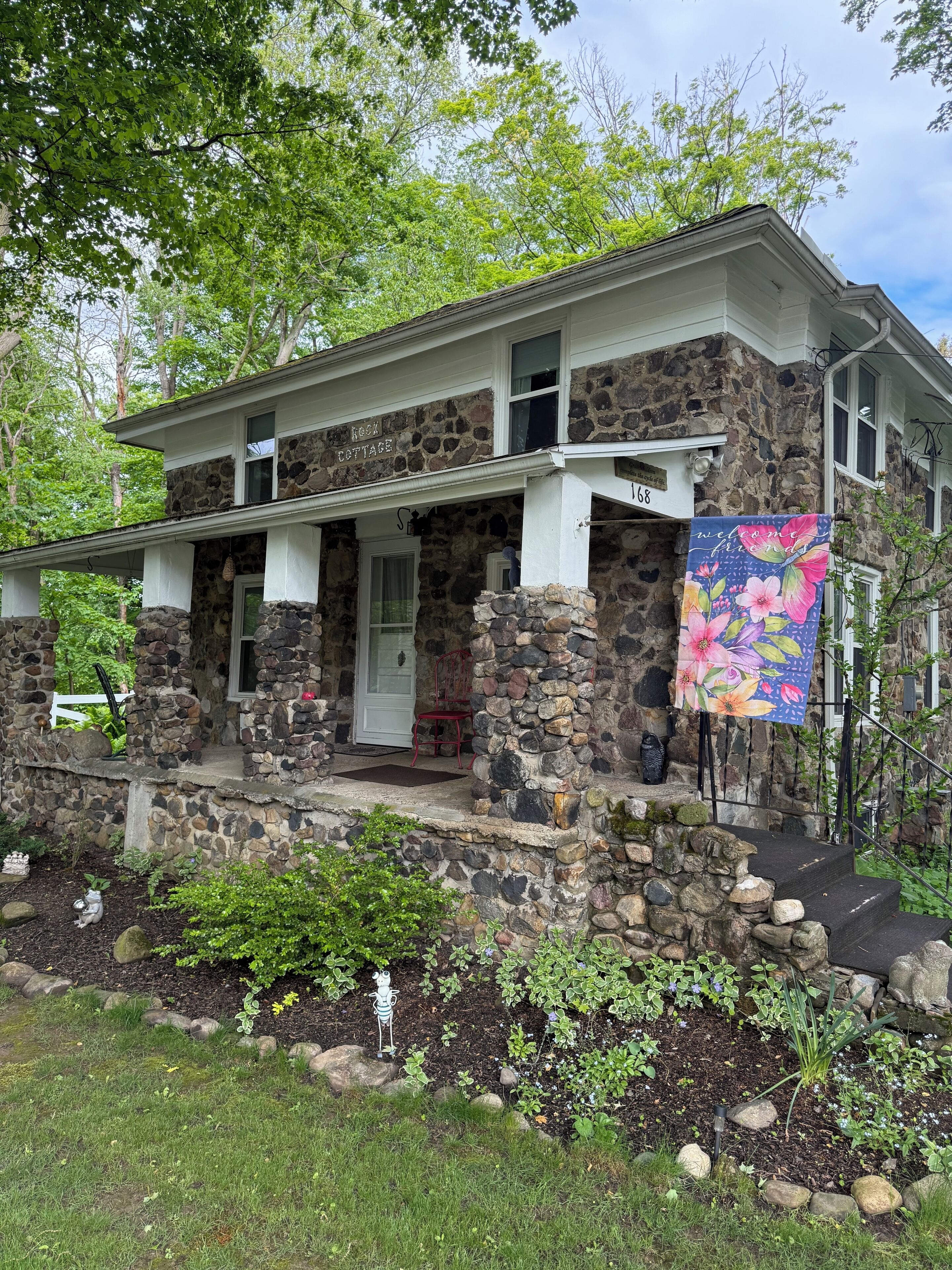 A stone house with a porch, a welcome sign, and a mailbox.