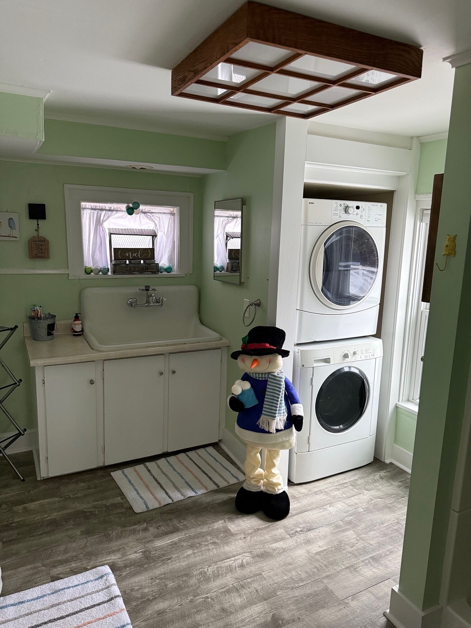 A laundry room with a washing machine, a dryer, a sink, and a small window with curtains.