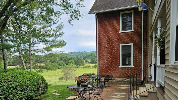 A brick house with a patio, outdoor seating, and a view of a green landscape. - The Serene Farm Life...without all the work!  Lots of space and privacy! (Buchanan)