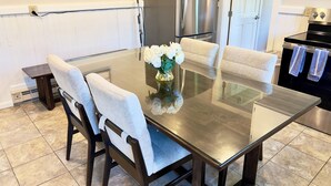 A modern kitchen with a glass-top dining table, four upholstered chairs, a stainless steel refrigerator, and a black oven. - Relax and unwind in our 4 bedroom beach condo. (Old Orchard Beach)