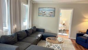 A living room with a sectional sofa, a round coffee table, and a painting of birds on the wall. - Relax and unwind in our 4 bedroom beach condo. (Old Orchard Beach)