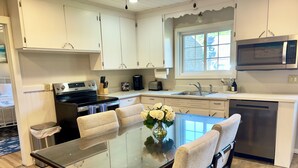 A modern kitchen with white cabinets, stainless steel appliances, a glass dining table, and a vase of white flowers. - Relax and unwind in our 4 bedroom beach condo. (Old Orchard Beach)