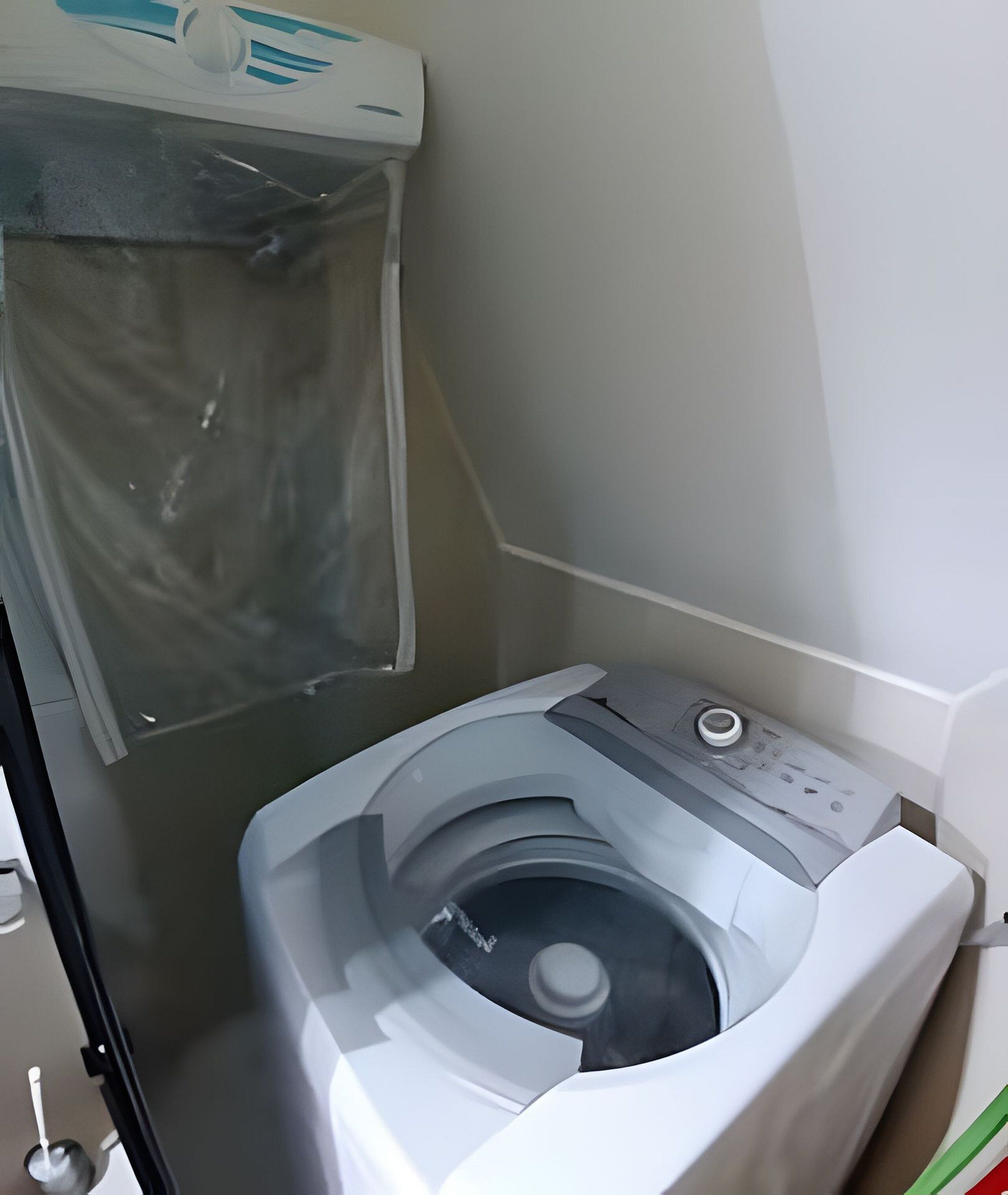 A compact, white washing machine in a small laundry room with a plastic bag hanging on the wall.