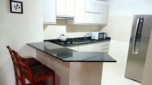 A kitchen with a central island, white cabinets, a microwave, and a refrigerator. - Siga Gramado-Casa de Vó c TVsmart e Wifi (Gramado)