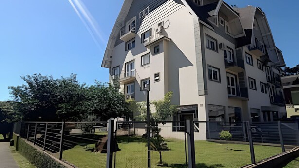 A multi-story residential building with a sloped roof, multiple balconies, and a gated entrance. - Siga Gramado-Casa de Vó c TVsmart e Wifi (Gramado)