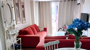 A living room with a red sofa, a round dining table, and a white chair. There is a vase with blue flowers on the table. - Siga Gramado-Casa de Vó c TVsmart e Wifi (Gramado)