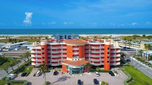 Un hotel de varios pisos con un patio central, rodeado por un estacionamiento y vistas a la playa.