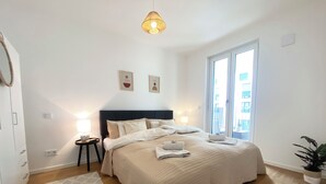 A bedroom with a large bed, bedside lamps, a small table, a potted plant, and a view of the outside. - Luxurious 2-room apartment, WLAN, washing machine (Schönefeld)