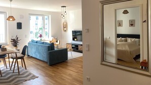 A modern living room with a sofa, dining table, and chairs. There is a TV and a plant on the table. - Luxurious 2-room apartment, WLAN, washing machine (Schönefeld)