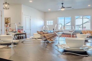 A dining area with a wooden table set for a meal, white bowls, wine glasses, and a decorative glass centerpiece. - Junction Escape: Pet Friendly + Office Space (Grand Junction)