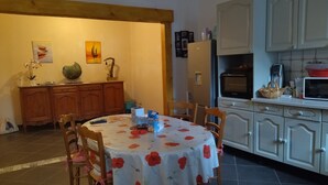 Ein Essbereich mit einem runden Tisch, der mit einer blumigen Tischdecke bedeckt ist, Holzstühlen, einem Holzschrank und einem Kühlschrank.