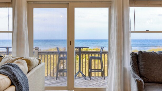 A room with a view of the beach through a glass door, a wooden deck, and a sofa. - Sleeps 28 Beachfront w/ Pool, Hot Tub, Game Room Atlantic Watch by Avantstay (Kill Devil Hills)