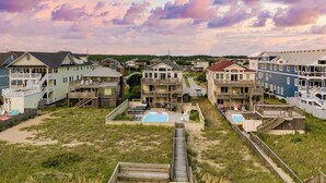 A beachfront residential area with multiple houses, a wooden boardwalk, and a swimming pool. - Sleeps 28 Beachfront w/ Pool, Hot Tub, Game Room Atlantic Watch by Avantstay (Kill Devil Hills)