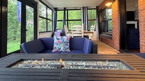 A covered outdoor seating area with a fire feature, a ceiling fan, and large windows.
