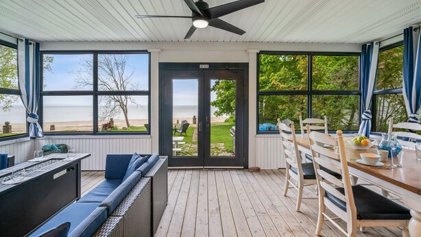 A covered outdoor dining area with a view of the beach, a ceiling fan, and a table set for dining.