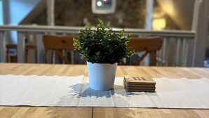 Een houten tafel met een witte tafelkleed, een kleine plant in een pot en een stapel kaarten.