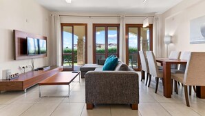 Una sala moderna con televisor de pantalla plana, un sofá, una mesa de comedor con sillas y un ventanal con vistas al exterior.