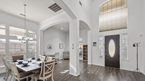 A spacious dining area with a long table, white chairs, and a chandelier. - Keller’s Crown - Huge House Near Stadiums - Hot Tub & Pool Table (Keller)