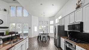 A modern kitchen with white cabinets, a granite countertop, stainless steel appliances, and a central island with stools. - Keller’s Crown - Huge House Near Stadiums - Hot Tub & Pool Table (Keller)