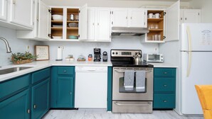Una cocina moderna con gabinetes verde azulado, una estufa de acero inoxidable y un lavavajillas blanco.