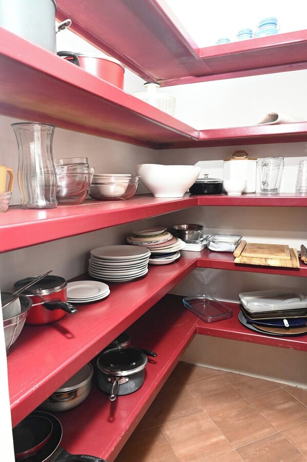 Una cocina con estantes rojos que contienen diversos utensilios de cocina, incluyendo platos, tazones y ollas.