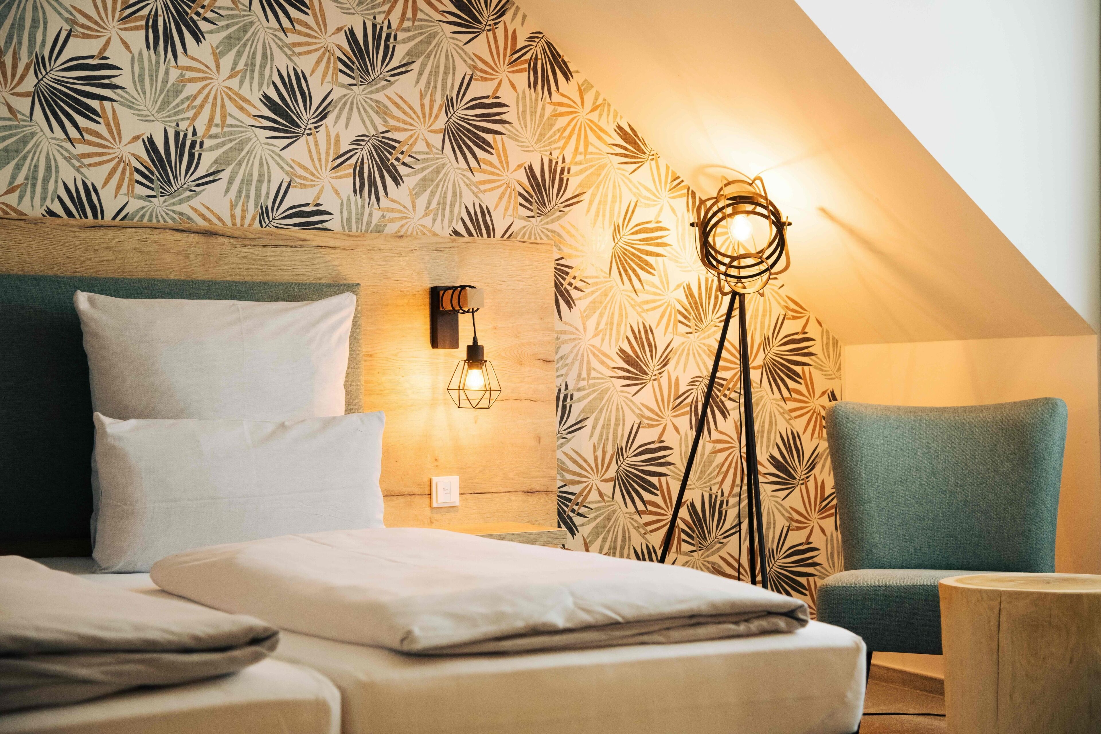 A bedroom with a bed, a chair, a wall-mounted light, and a patterned wallpaper.