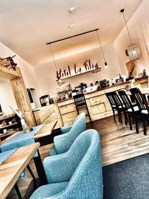 A modern hotel interior with a central dining area, wooden furniture, and a visible reception desk. - Hotel Le Filou  (Hille)