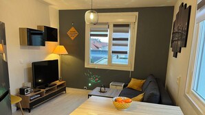 Un salon moderne comprenant un téléviseur, un canapé, une table à manger et une fenêtre avec des stores.