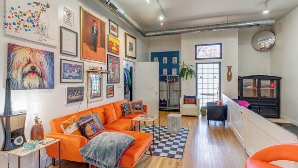 A modern living room with an orange sofa, a checkered rug, and various artworks on the walls. - Animal House Near Sox Stadium (Chicago)