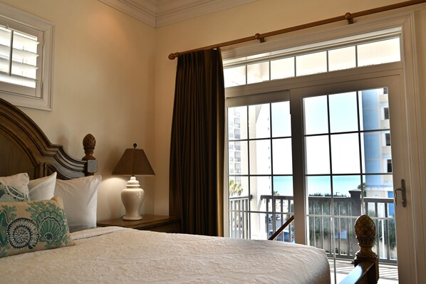 Habitación de hotel con una cama grande, una mesita de noche con lámpara, una ventana con cortinas y vistas al balcón exterior.