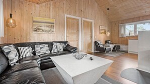 A modern living room with a leather sofa, a white coffee table, and two armchairs. Wooden paneling and a large window are visible. - Nice home in Nørre Nebel with sauna (Nørre Nebel)