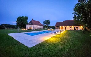 A swimming pool with a paved deck, surrounded by a grassy lawn and two buildings with red roofs. - Cozy home in Aresches (Aresches)