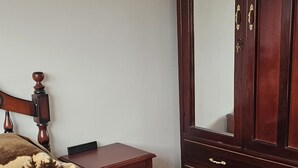 Ein Schlafzimmer mit einem Bett, einem Holzschrank, einem kleinen Tisch und einem Spiegel.