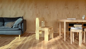 Une pièce avec un plancher en bois, un canapé bleu avec des coussins, une chaise en bois, une petite table en bois sur laquelle se trouvent un livre et un vase.