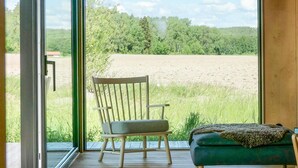Une pièce avec une chaise en bois et un pouf vert, près d’une grande fenêtre donnant sur un champ.