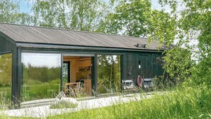 Une maison moderne dotée de grandes baies vitrées, d’un revêtement extérieur en bois et offrant une vue sur la verdure environnante.