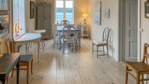 Un comedor con una mesa y sillas de madera, una ventana con vista al agua, y una puerta a la derecha.