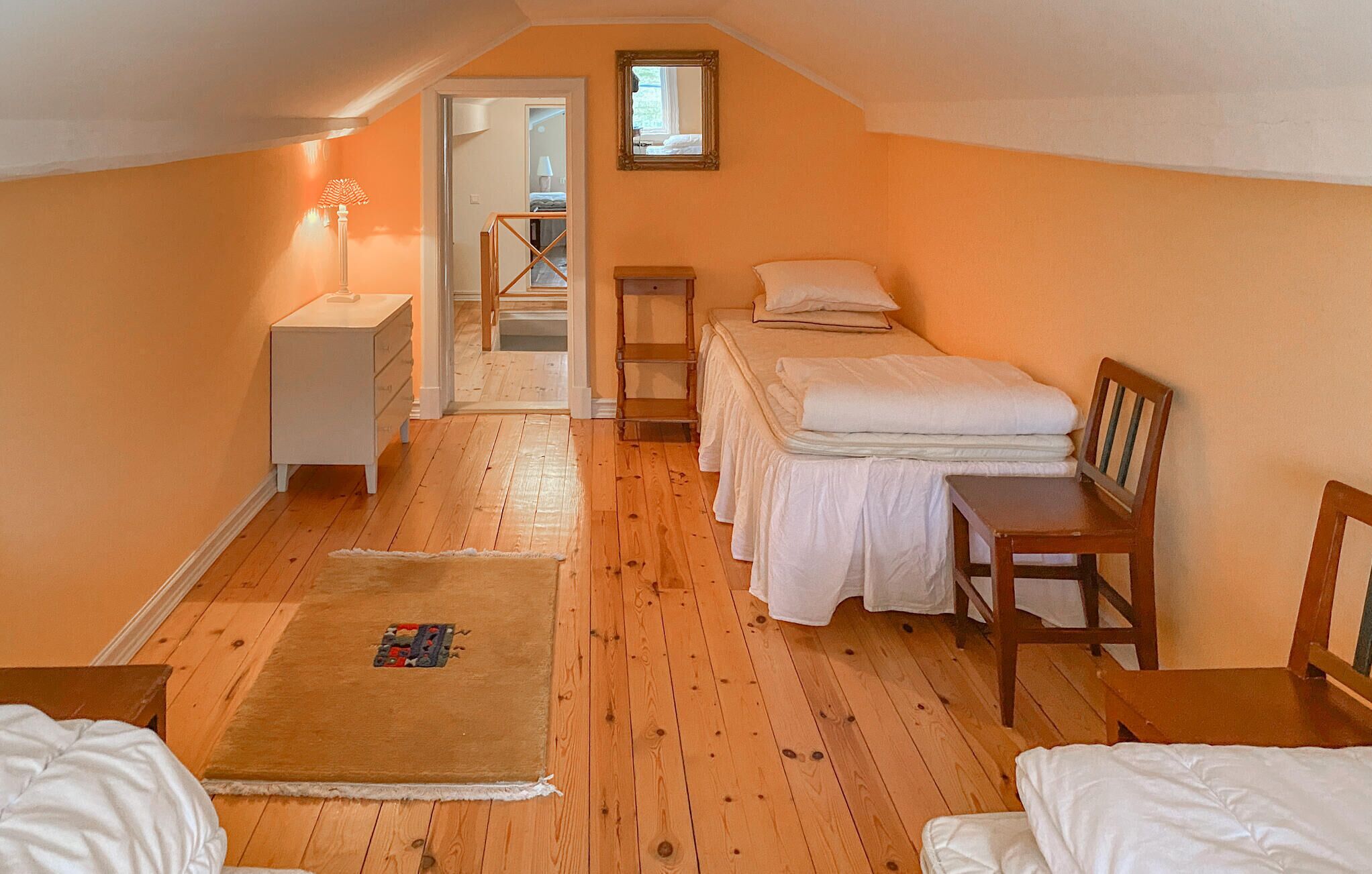 A bedroom with a wooden floor, two beds, a nightstand, a dresser, a chair, and a small table.