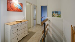 Un couloir avec une commode blanche, un tableau et une porte donnant sur une autre pièce.