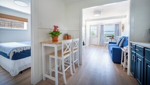 A bright, open-plan living area with a bed, a dining table with chairs, a blue sofa, and a view through an open doorway. - Private Two-Bedroom Cottage (Waterford)