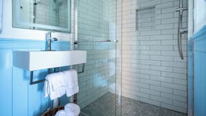 A modern bathroom with a glass shower enclosure, white tiled walls, and a blue vanity. - Private Two-Bedroom Cottage (Waterford)