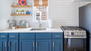 A kitchen with blue cabinets, a stove, and a window above the sink. - Private Two-Bedroom Cottage (Waterford)