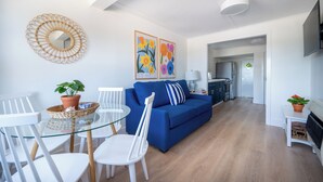 A modern living room with a blue sofa, white chairs, a glass table, and a mirror on the wall. There are two framed floral paintings above the sofa. - Private Two-Bedroom Cottage (Waterford)