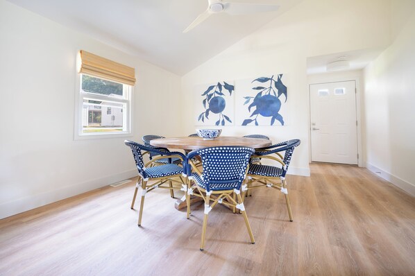 A dining area with a round table and six chairs, a ceiling fan, and artwork on the walls.