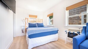 A bedroom with a bed, a blue chair, a small table, and a window with blinds. - Private Cottage at Marina Bay (Waterford)