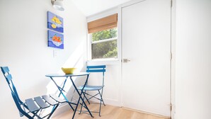 A room with a window, a table with a bowl, two blue chairs, and two wall-mounted paintings. - Private Cottage at Marina Bay (Waterford)