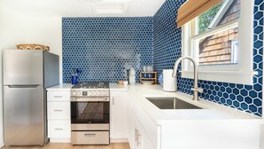A modern kitchen with white cabinetry, a stainless steel refrigerator, a gas stove, and a sink. - Private Cottage at Marina Bay (Waterford)